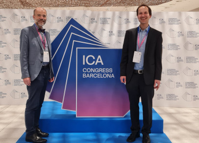 Das Bild zeigt Dr. Florian Lehrmann und Prof. Dr. Thomas Henne vor einem Aufsteller zum ICA-Kongress in Barcelona