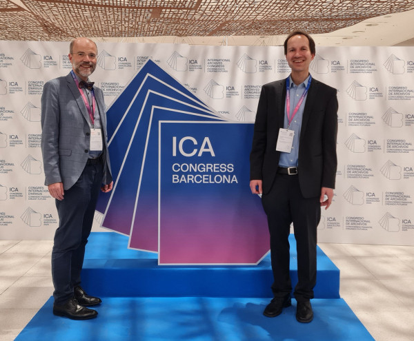 Das Bild zeigt Dr. Florian Lehrmann und Prof. Dr. Thomas Henne vor einem Aufsteller zum ICA-Kongress in Barcelona