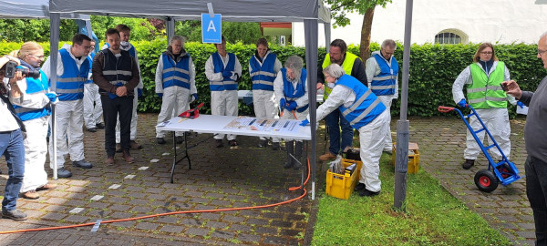 Mehrere Menschen in Westen stehen in einem offenen Zelt um einen Tisch.